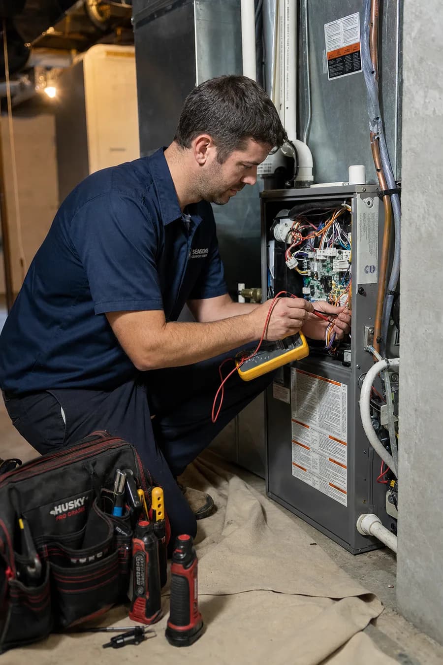 HappyVac technician testing a furnace control board with a multimeter